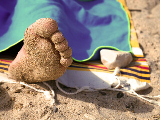 Foot in the sand. Person lying on the beach on a towel. Summer sunny day. Holiday at the sea. Calm, happy, joyful mood. Perfect for poster, advertisement, postcard