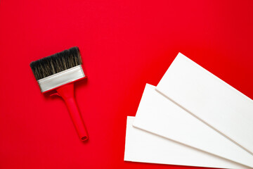 A large new red paintbrush in metal edging with a plastic handle for painting and three white wood planks on a red background. Christmas banner with copy space for a hardware store or art shop