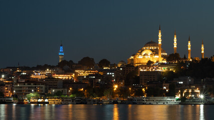 Naklejka premium Istanbul-September 23, 2020. Evening view of the Suleymaniye mosque, across the Golden horn Bay. Mosque and buildings on the shore in the lights that are reflected in the night water of the Bay.