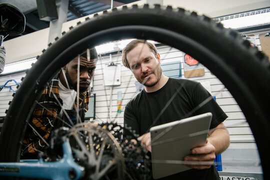 Male bike shop mechanics with digital tablet fixing bicycle