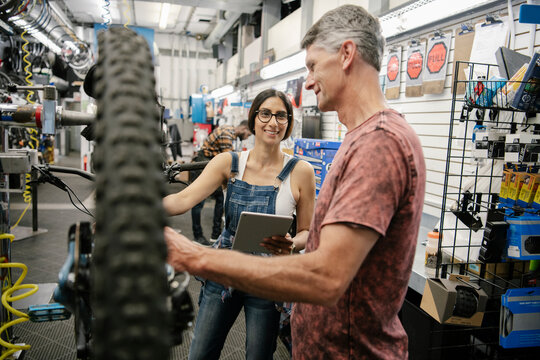 Bike shop mechanics with digital tablet repairing bicycle in workshop