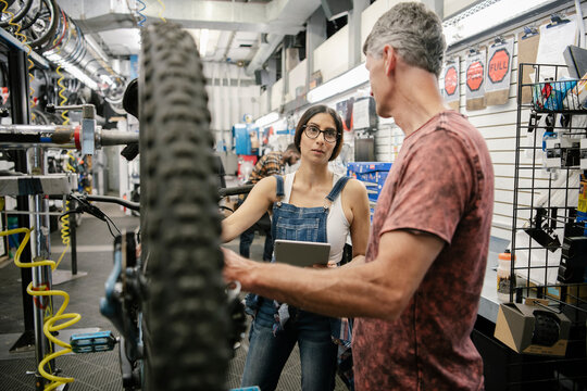 Bike shop mechanics with digital tablet fixing bicycle in workshop
