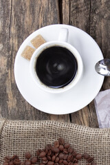 A white cup of coffee on a wooden background. Coffee beens on a linen fabric. Breakfast coffee