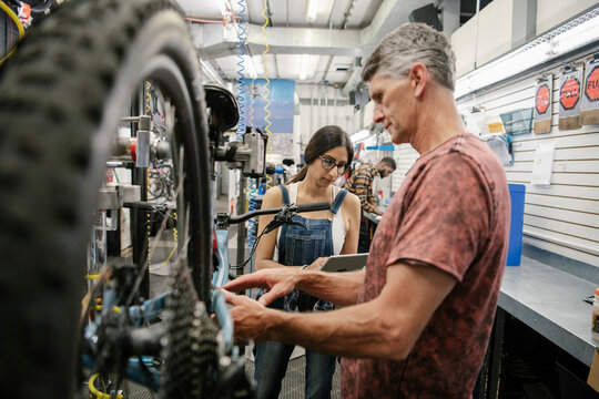 Bike shop mechanics with digital tablet repairing bicycle in workshop