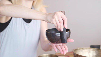 Woman playing on Tibetan singing bowl while sitting on yoga mat. Vintage tonned.