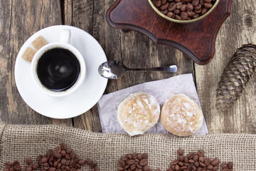 A white cup of coffee and cake on a wooden background. A coffee grinder and coffee beens on a linen fabric. Cone