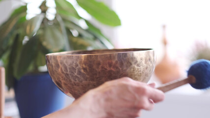 Woman playing on Tibetan singing bowl while sitting on yoga mat. Vintage tonned.