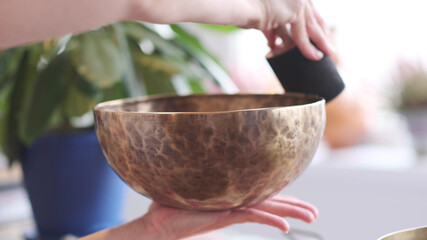 Woman playing on Tibetan singing bowl while sitting on yoga mat. Vintage tonned.