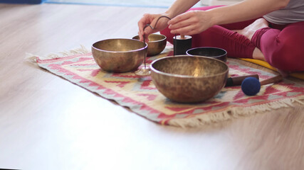 Woman playing on Tibetan singing bowl while sitting on yoga mat. Vintage tonned.