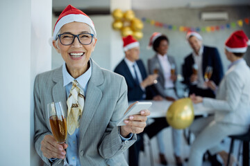Happy mature businesswoman using mobile phone at New Year's party in the office.