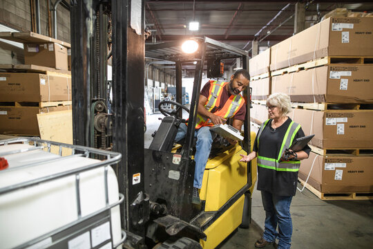 Warehouse owner checking forklift driver moving stock
