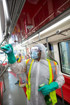Male transit worker in subway sanitizing subway handle