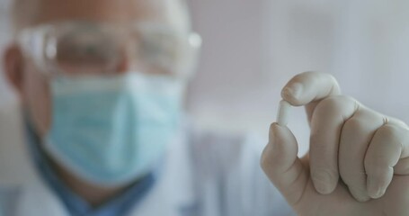 Extreme Close-up of a masked scientist developing a coronavirus vaccine holding a white pill. The doctor looks at the painkillers antiviral medication. Vitamins - Powered by Adobe