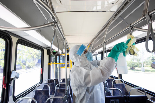 Male worker in clean suit sanitizing public bus