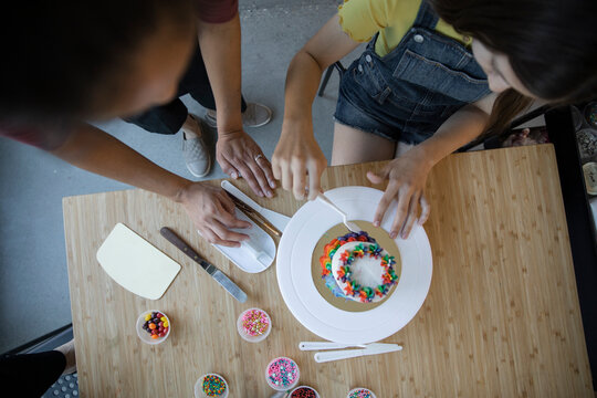 Woman Teaching Teen Girl To Decorate Cake Overhead View