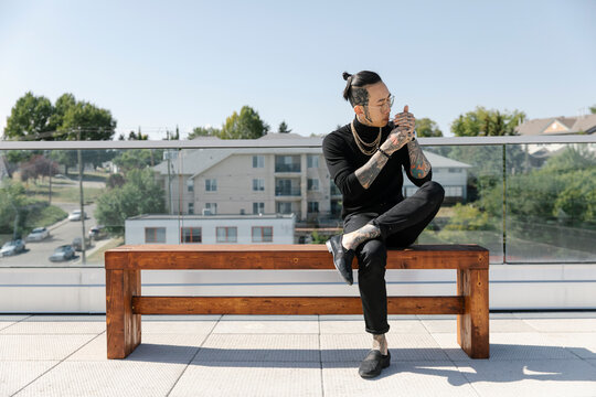 Asian Man Sitting On Bench Lighting Cigarette