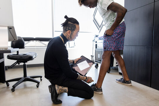 Tattoo artist looking at customer's leg in studio