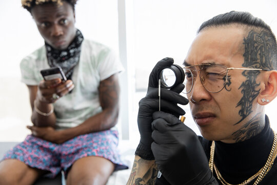 Customer Watching Tattoo Artist Check Needle With Magnifying Glass