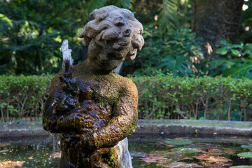 Fototapeta na wymiar Estatua o escultura de niño en una fuente en el Jardin Botanico Historico de La Concepcion en Malaga, Costa del Sol, Andalucia, España