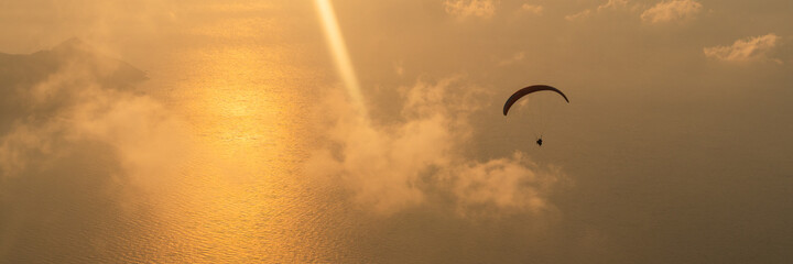 Silhouette of paraglider soaring over sea at sunset light. Wide banner