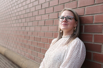 Beautiful, Young 30 Years Old Girl with Blonde Hair, in Glasses, wearing white dress, Smiling and Posing for camera, red Bricks background, Happy Woman  