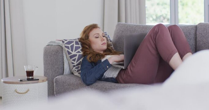 Woman using laptop while lying on the couch at home