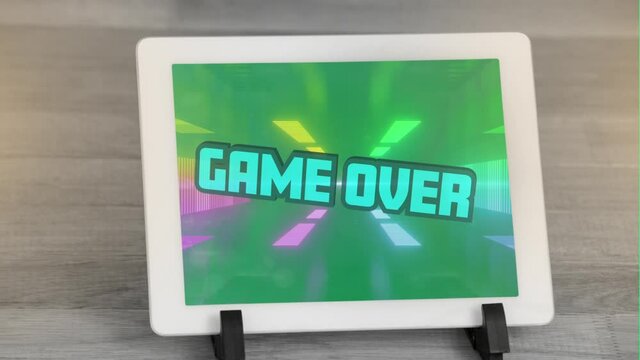 Digital animation of game over text against glowing tunnel on screen of digital tablet on wooden sur