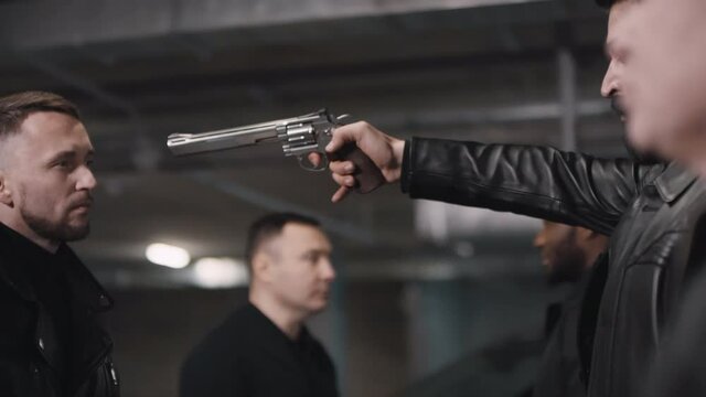 Criminals having illegal deal at underground parking and arab leader pointing at another bandit with pistol looking angrily