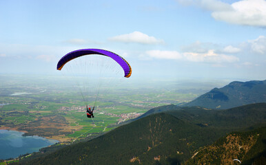 Paraglider pilot on purple paraglider flies from Mount Tegelbergbahn in Germany over a beautiful...
