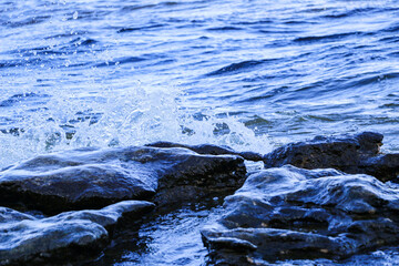 waves run onto the shore and crash against the rocks, creating many splashes and splashes near the shore. river surf in stormy weather near a stone pebble coast with foamy splashing waves.