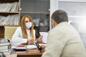 Middle aged woman office manager in protective mask communicates with visitor at meeting in office