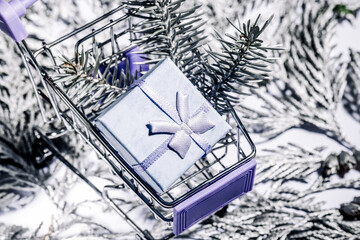 A shopping cart  trolley with christmas and new year gift  on silver thuja branches, Christmas and New Year shopping. Winter sale