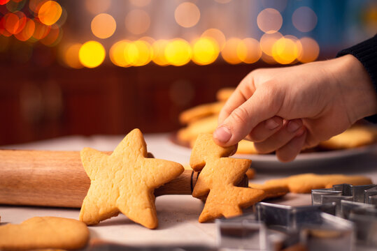 Cookies in star and christmas tree shapes on the table near rolling pin and baking accessories. Hand of a young boy showing homemade shortbread.