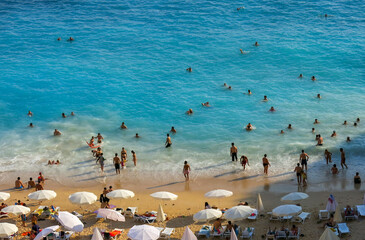 Famous Antalya Kaputas beach, close up photo while a lot of people are inside the wavy turquoise coloured sea and swimming.