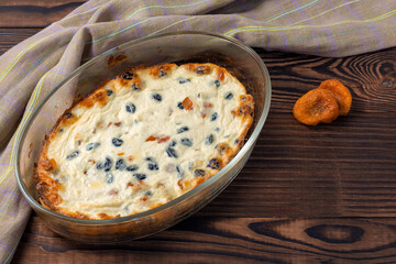 Oven baked homemade curd casserole with raisins and dried apricots on brown wooden background. Copy space