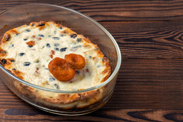 Oven baked curd casserole with raisins and dried apricots on brown wooden background. Copy space