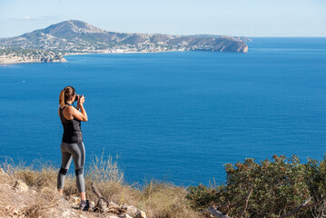 Woman taking pictures with her camera to the landscape, in nature from the Peñon de Ifach in Calpe