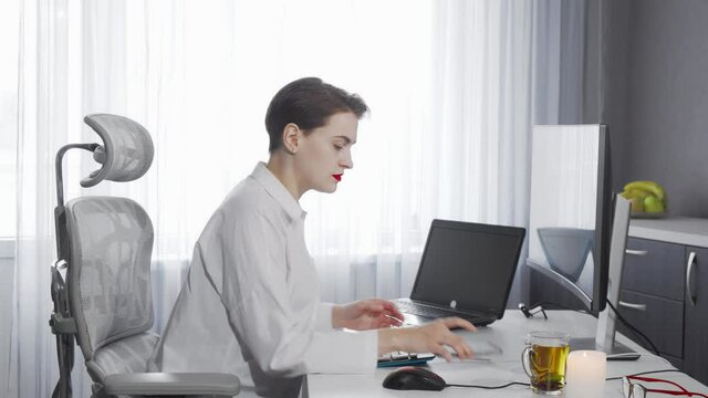 Female freelancer using her smart phone while working on a computer. Attractive young businesswoman working at her office. Female IT developer working on a project