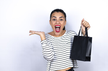 Fototapeta premium Young beautiful woman holding a black shopping bag crazy and mad shouting and yelling with aggressive expression and arms raised. Black Friday