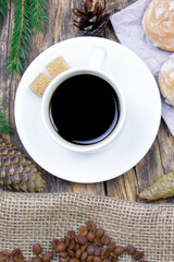 A white cup of coffee and cakes on a wooden background. Coffee beens on a linen fabric. Breakfast coffee. Fir branch