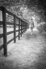 Thoughtful Woman Walking Away Along Fence Outdoors, Black And White