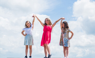 we are strong. sisterhood and friendship. family bonding time. best friends forever. three sisters on sky background. happy childhood. summer vacation. small girls hold hands. love and support