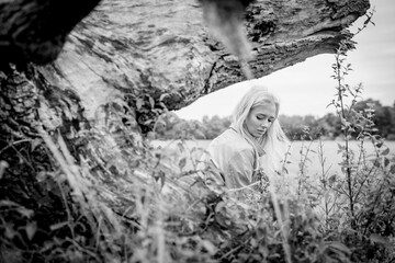 Young Woman Sitting On A Tree Outdoors In Long Grass In Black And White