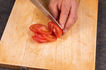 Tomatoes on wooden cutting board with visible part of hands of chef and a knife in action