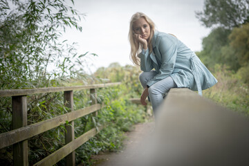 Naklejka na ściany i meble Thoughtful Young Woman Sitting On a Fence On A Bridge