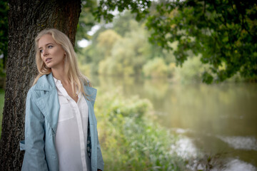 Young Woman Leaning Against A Tree By A River Looking Away