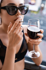 Sexy young woman in black underwear smoking cigarette and drinking wine on balcony