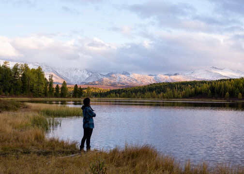 girl stands with her back near the lake, looks at a beautiful sunset in the mountains