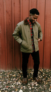 Man in green jacket and brown boots standing outside and sitting on stoop