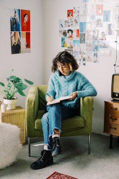 Trendy pensive teenager taking notes in diary while chilling at home